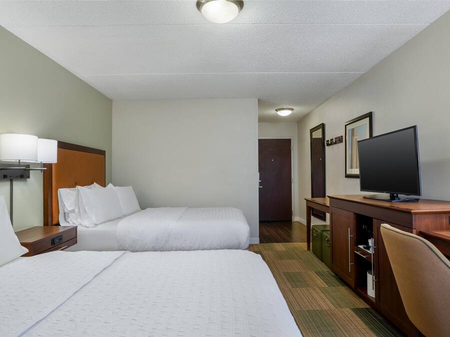 Habitación de hotel con dos camas, un escritorio, televisión, lámpara y una puerta que da a otra habitación.