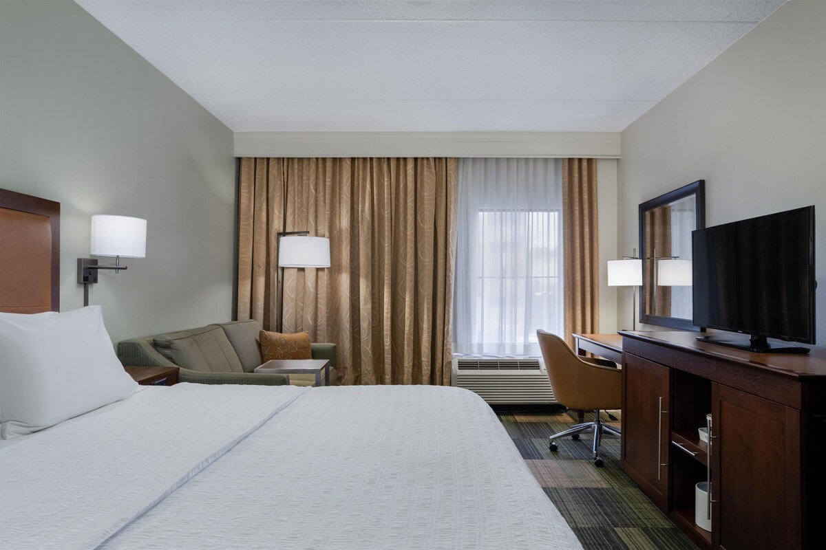 A hotel room with a bed, a desk, a chair, a television, and a window with curtains.