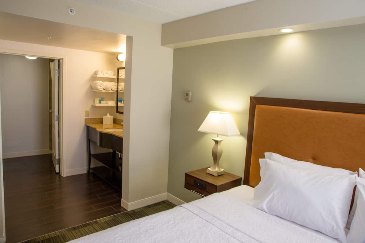 A hotel room with a bed, a nightstand with a lamp, a bathroom with a sink and towel rack.