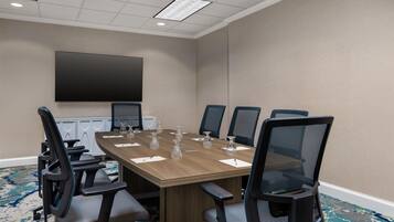 A conference room with a large table, six chairs, a flat-screen TV, and a carpeted floor.