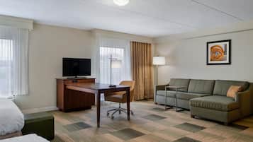 A hotel room with a bed, a desk with a television, a sofa, a chair, and a lamp.