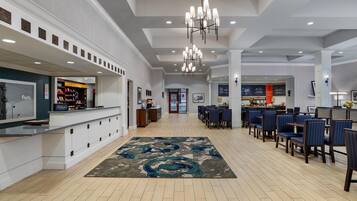 Un hall de hotel con mostrador de recepción, zona de estar y vistas a la cocina al fondo.