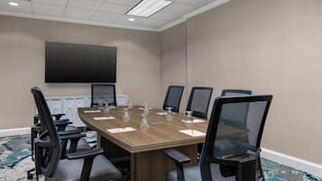 A conference room with a large table, six chairs, a flat-screen TV, and a carpeted floor.