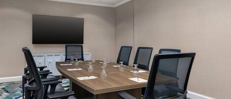 A conference room with a large table, six chairs, a flat-screen TV, and a carpeted floor.