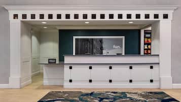A hotel reception area with a modern design, including a reception desk, a framed picture, and a selection of snacks on the right.