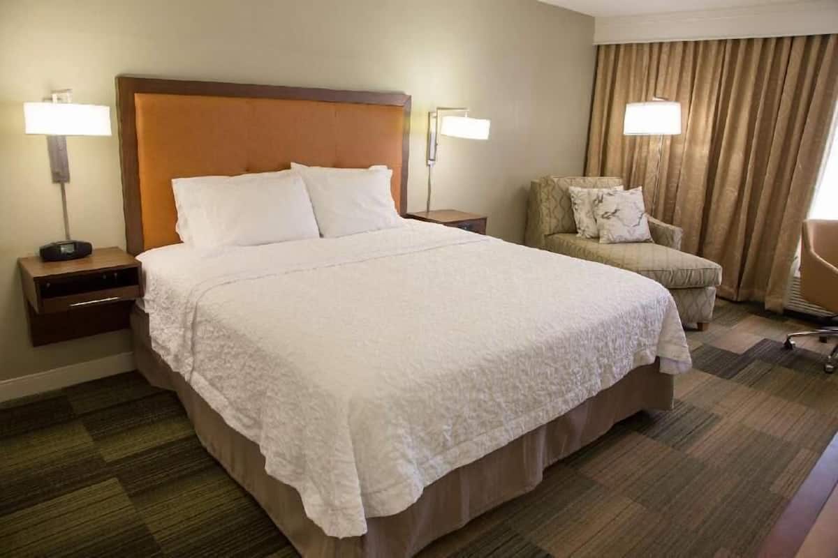 A hotel room with a large bed, two bedside tables, a chair, and a lamp.
