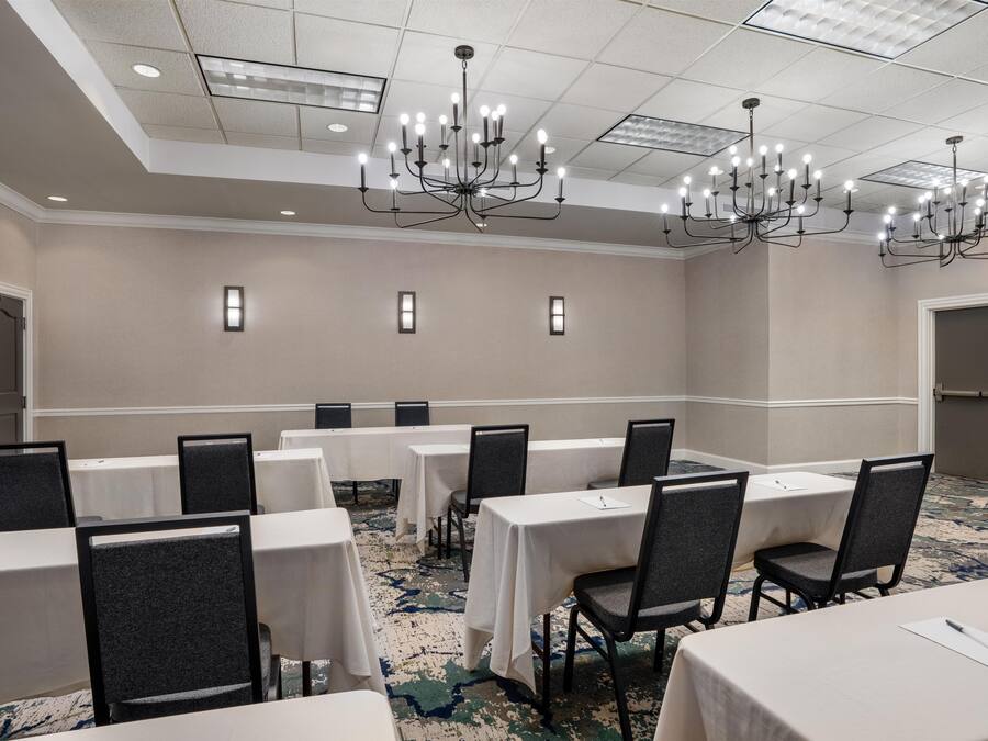Une salle de conférence dotée de plusieurs tables et chaises, d’un lustre et d’un sol recouvert de moquette.