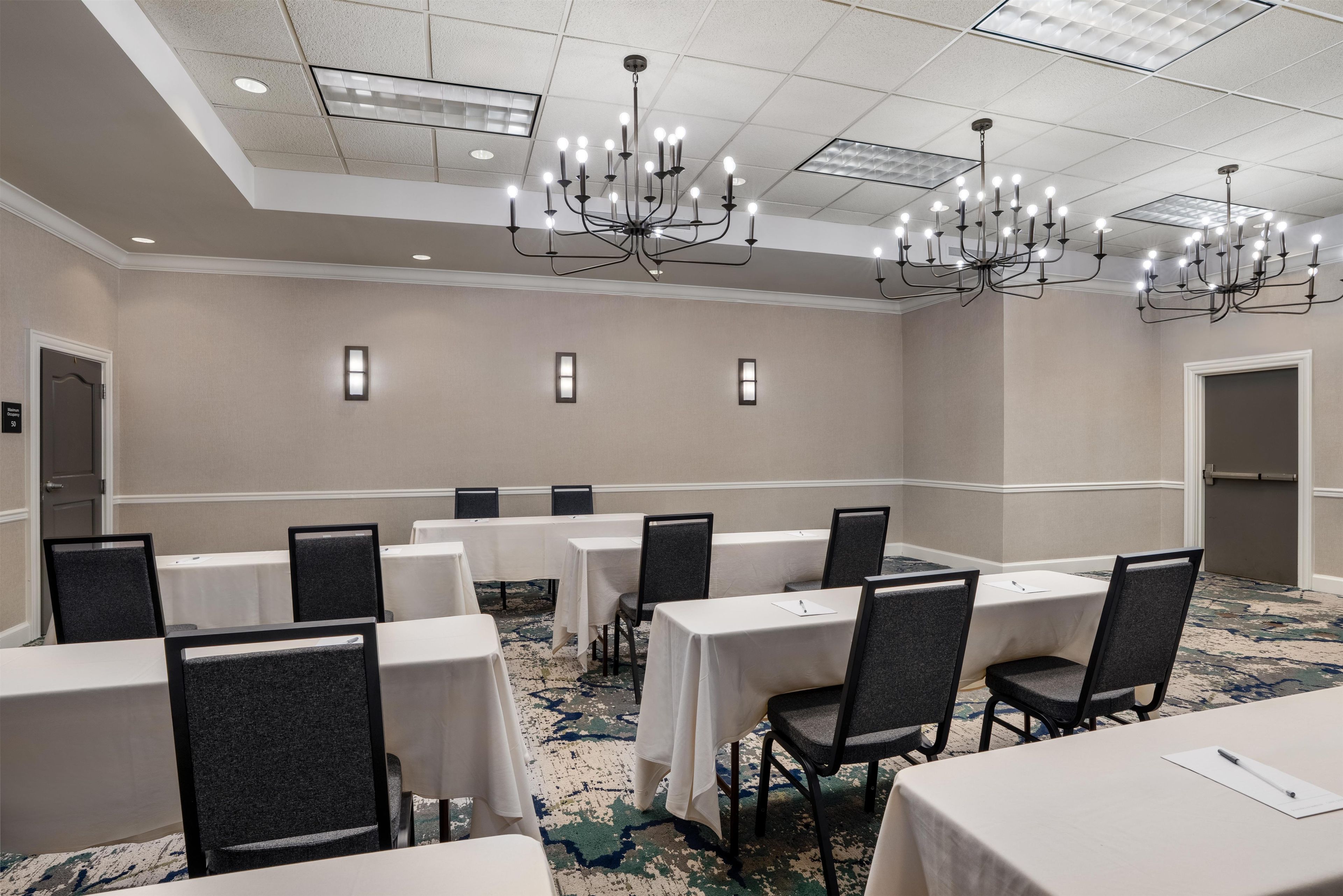 A conference room with multiple tables and chairs, a chandelier, and a carpeted floor.