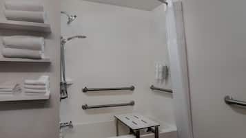 A modern bathroom with a shower, grab bars, a towel rack, and a small table.