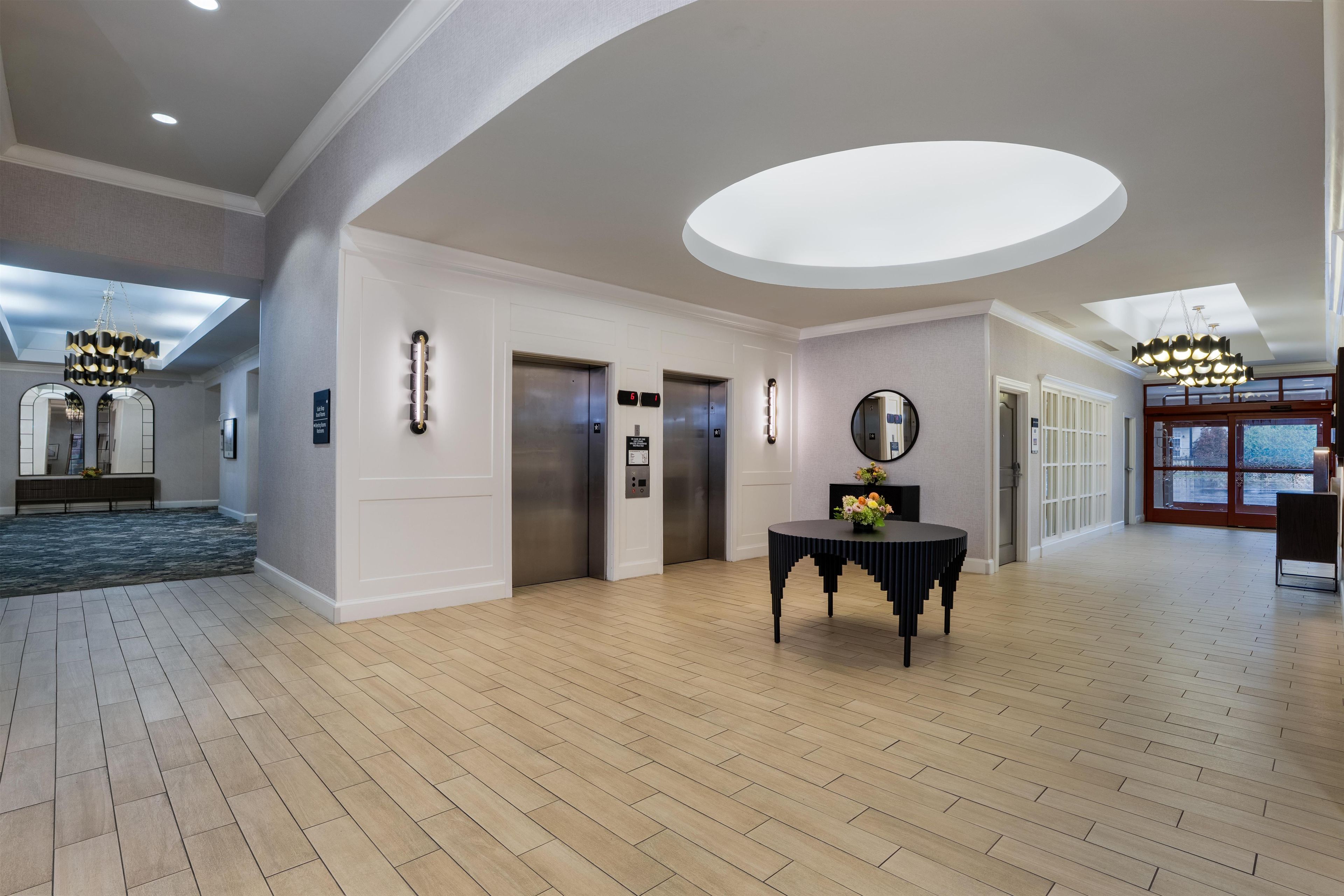 Um hall amplo com piso de madeira, uma mesa redonda com um vaso e um grande claraboia circular.
