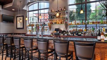 Una zona de bar con una barra alargada, varias opciones de asientos y vistas al exterior a través de amplios ventanales.