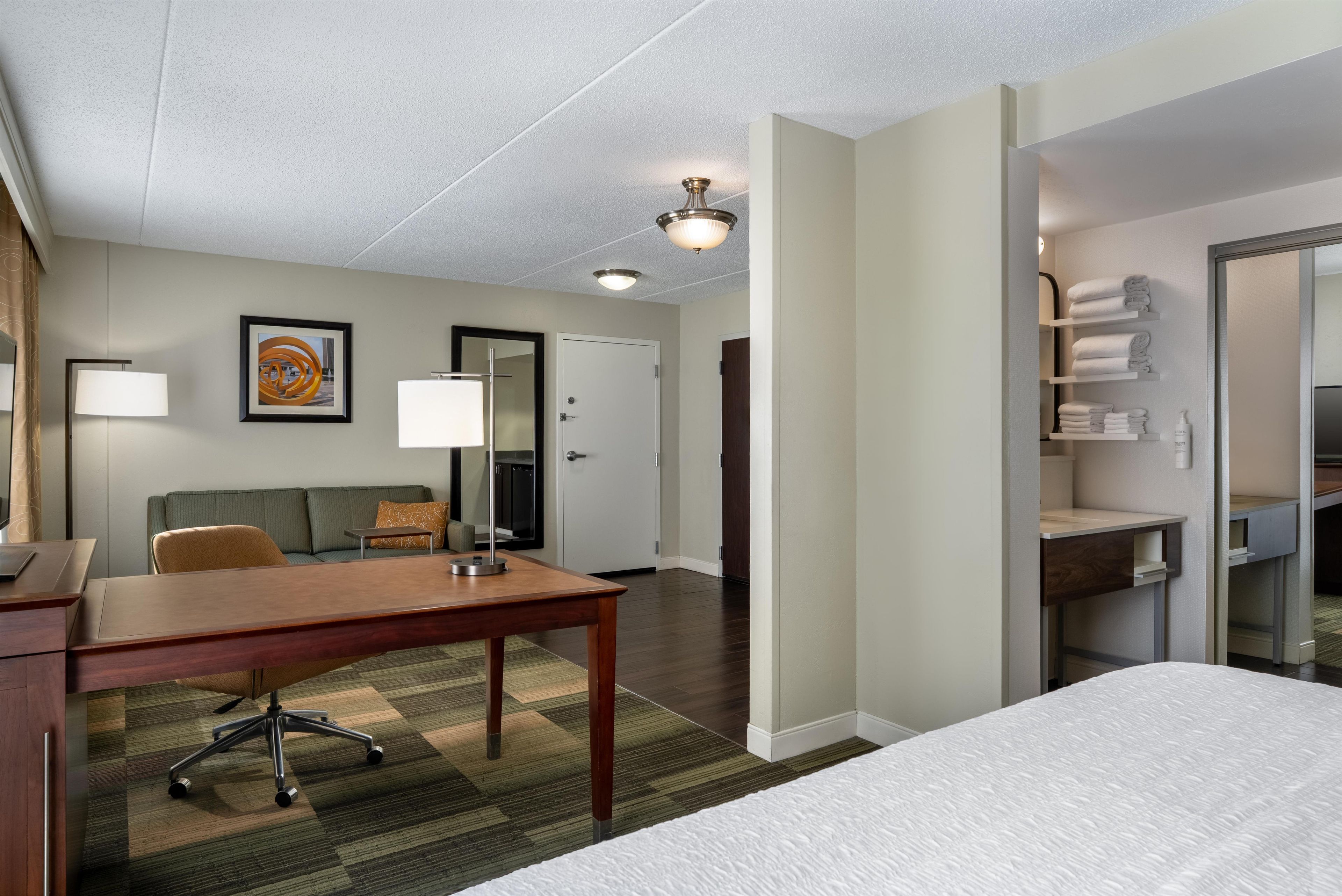 A hotel room with a bed, desk, chair, and a bathroom with shelves.