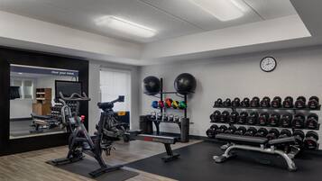 Un gimnasio con equipamiento de ejercicio, estantes para pesas y un espejo.