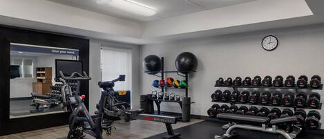 Un gimnasio con equipamiento de ejercicio, estantes para pesas y un espejo.