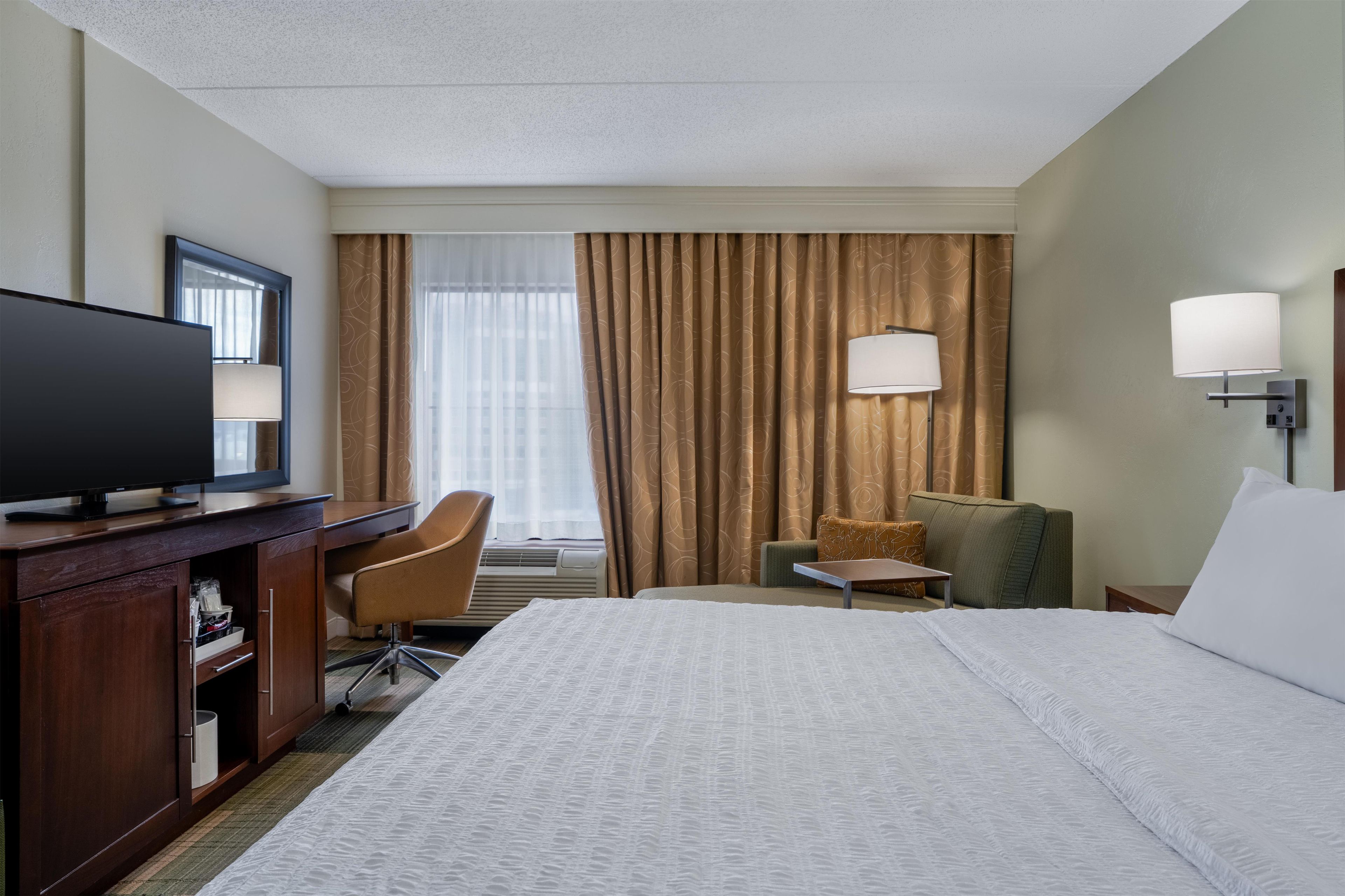 Une chambre d’hôtel comprenant un lit, un bureau avec une télévision, une chaise, une petite table et une lampe.