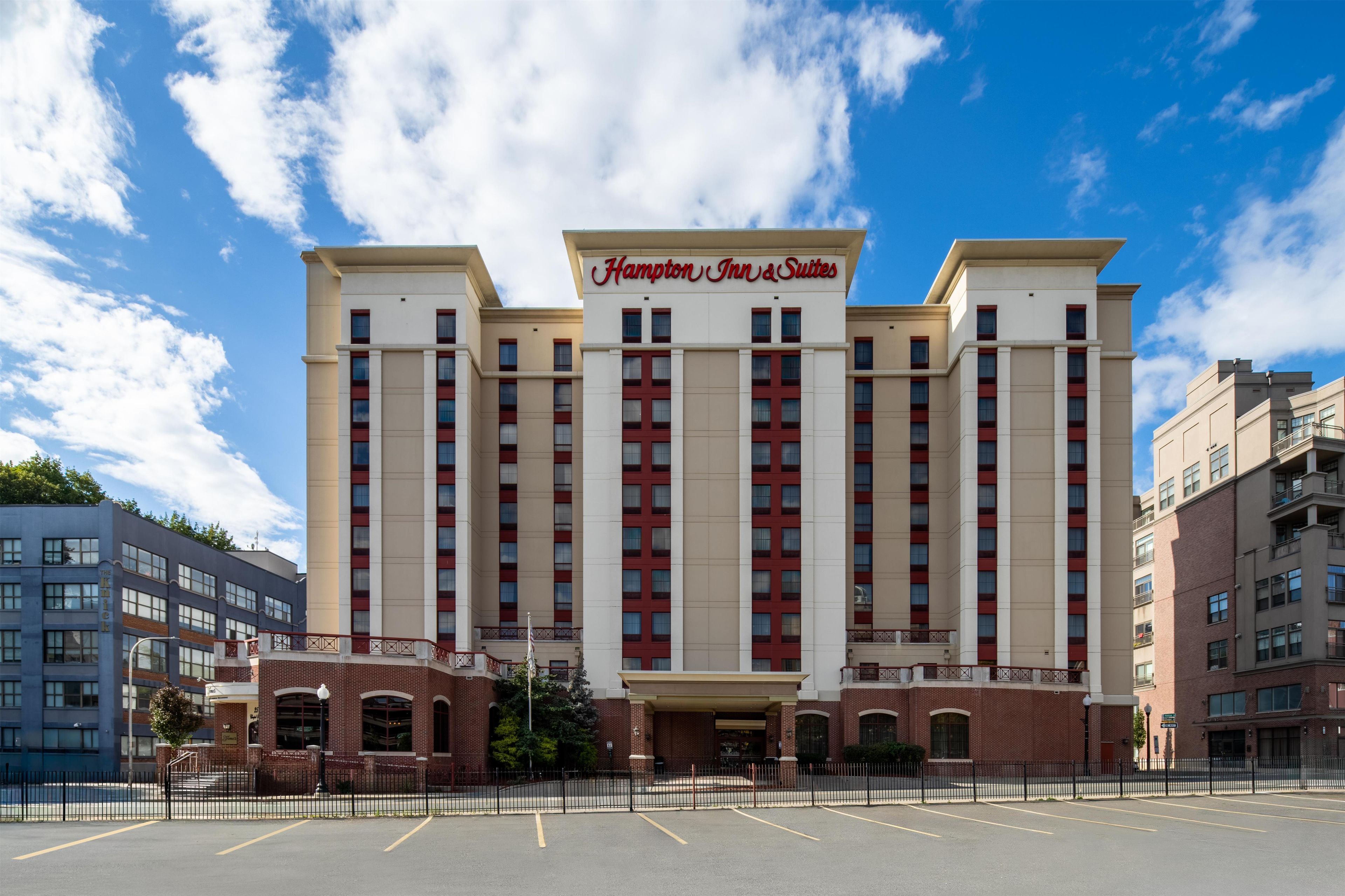 Un hotel grande de varios pisos con un letrero llamativo que dice 'Hampton Inn & Suites'.