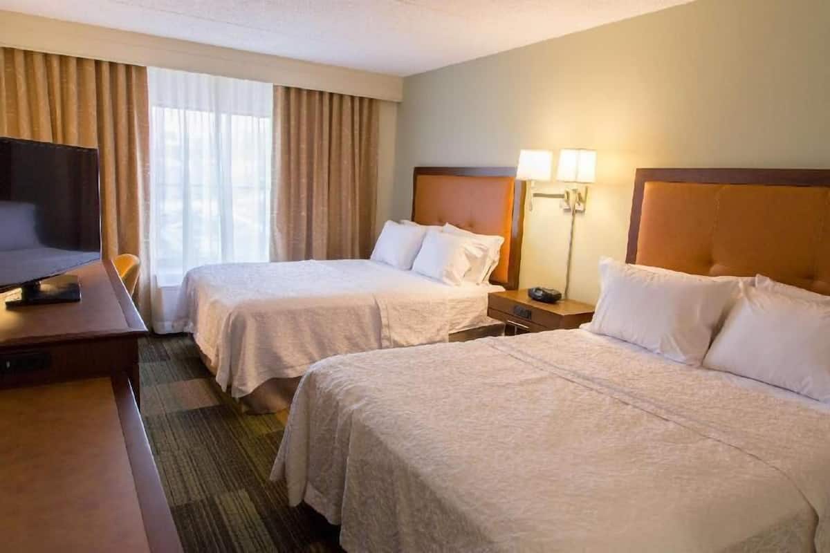 A hotel room with two beds, a desk with a television, and a window with curtains.