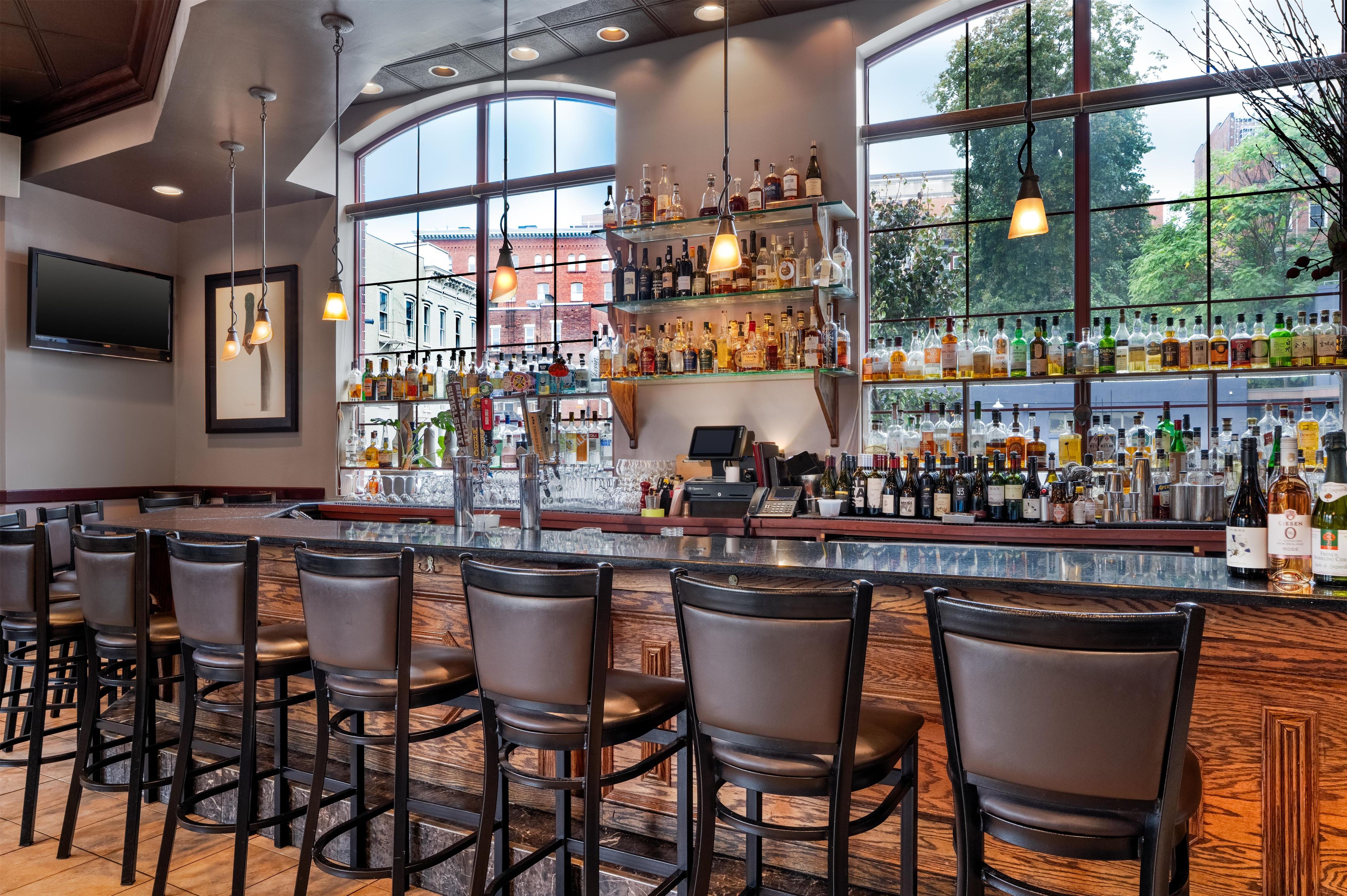A bar area with a long counter, multiple seating options, and a view of the outside through large windows.