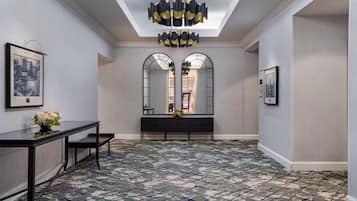 A hallway with a patterned floor, a console table with a vase of flowers, and a large mirror.