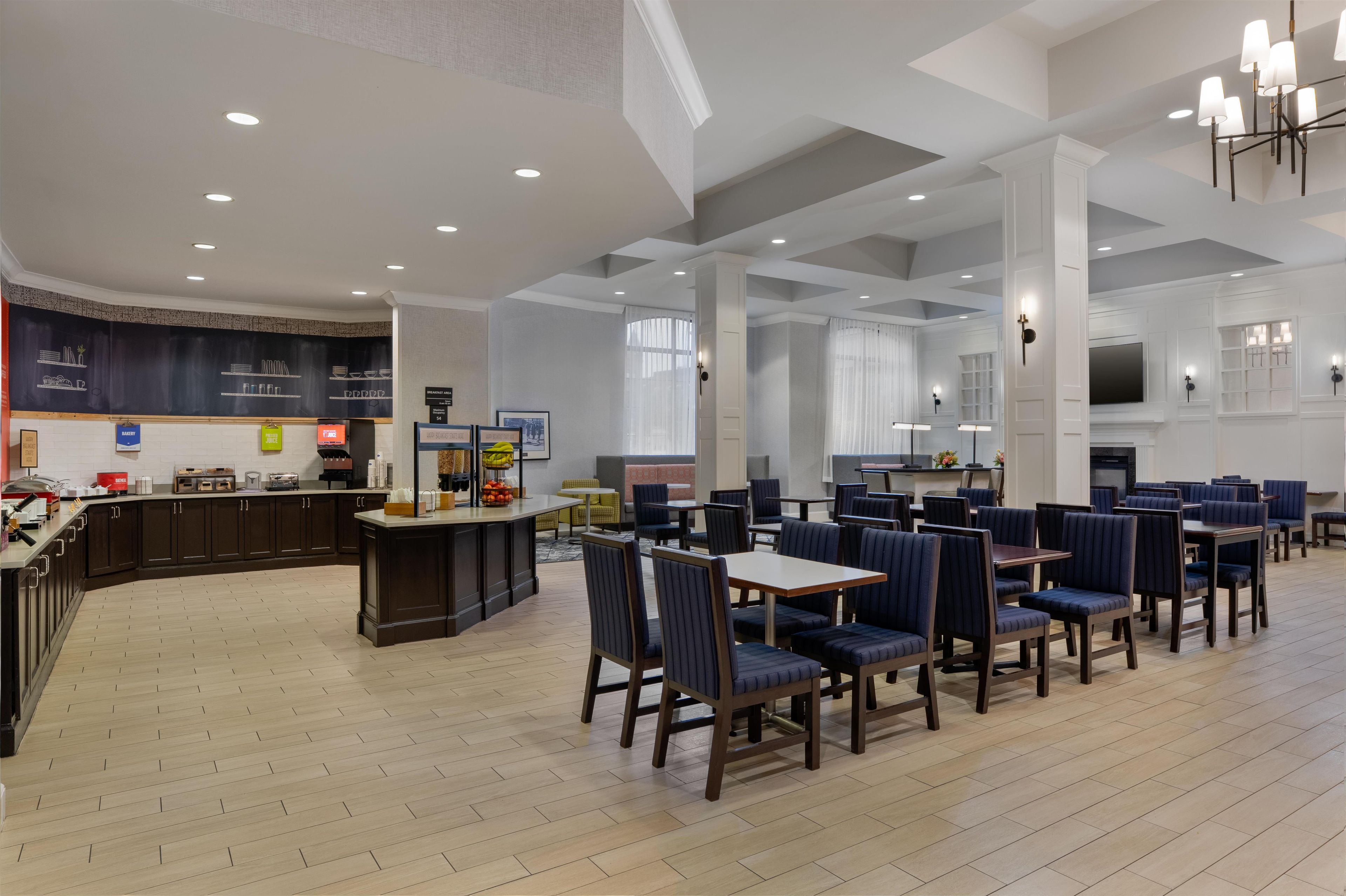 Un amplio comedor de hotel con techos altos, un bar central y diferentes distribuciones de mesas.