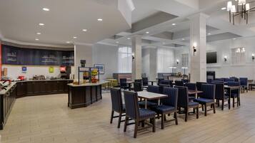 Un amplio comedor de hotel con techos altos, un bar central y diferentes distribuciones de mesas.