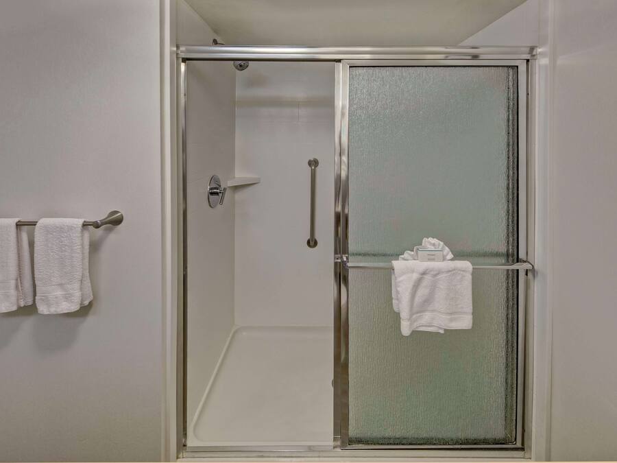 A glass-enclosed shower with a door handle and a towel rack with two towels.