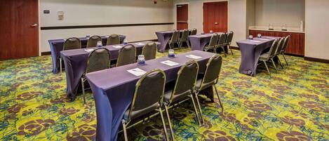Un salón de conferencias con varias mesas y sillas, suelo alfombrado y puertas.