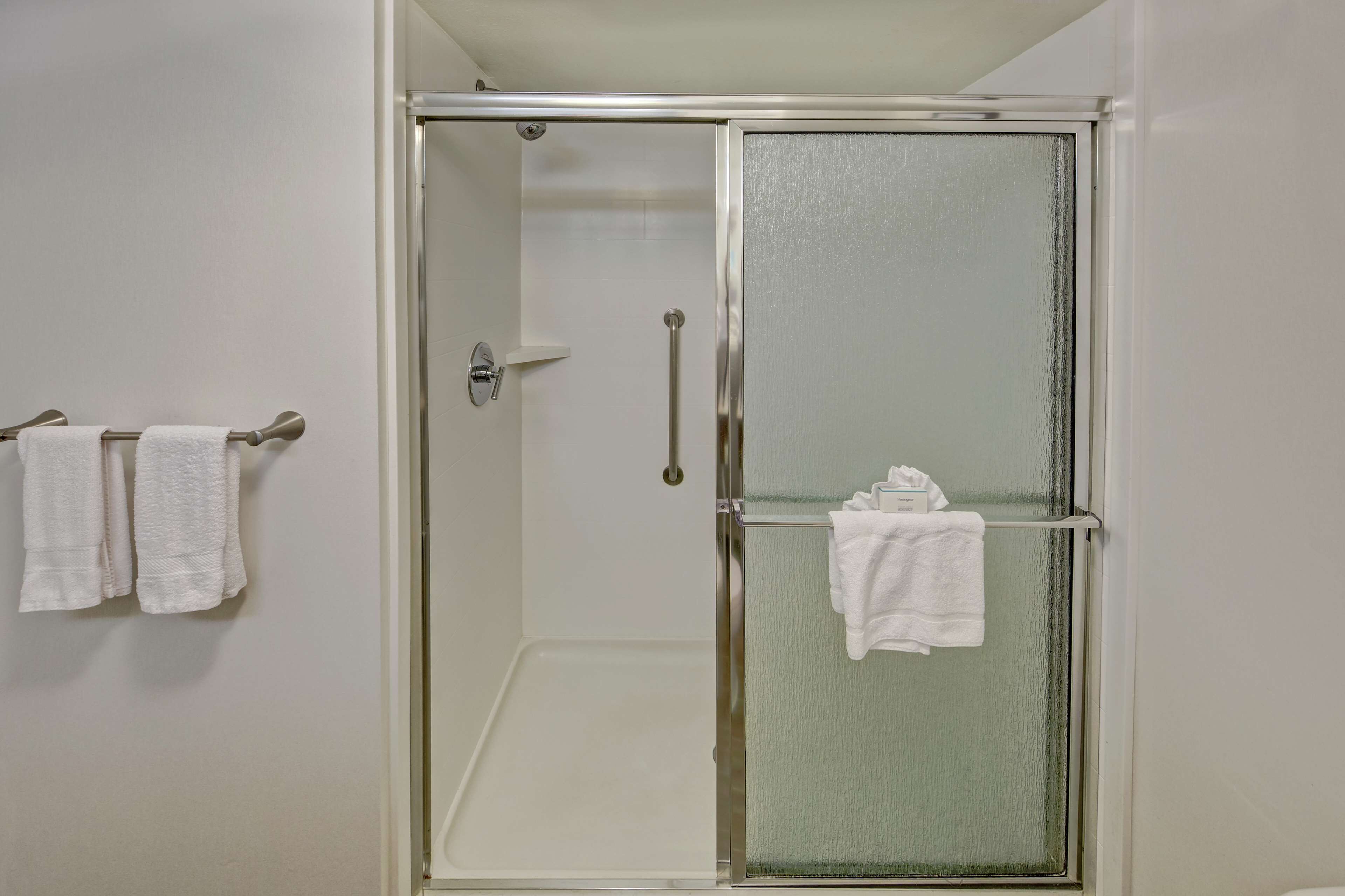 A glass-enclosed shower with a white interior, a towel rack with two towels, and a glass door with a handle.