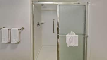 Una ducha con cerramiento de vidrio, interior blanco, un perchero con dos toallas y una puerta de vidrio con manija.