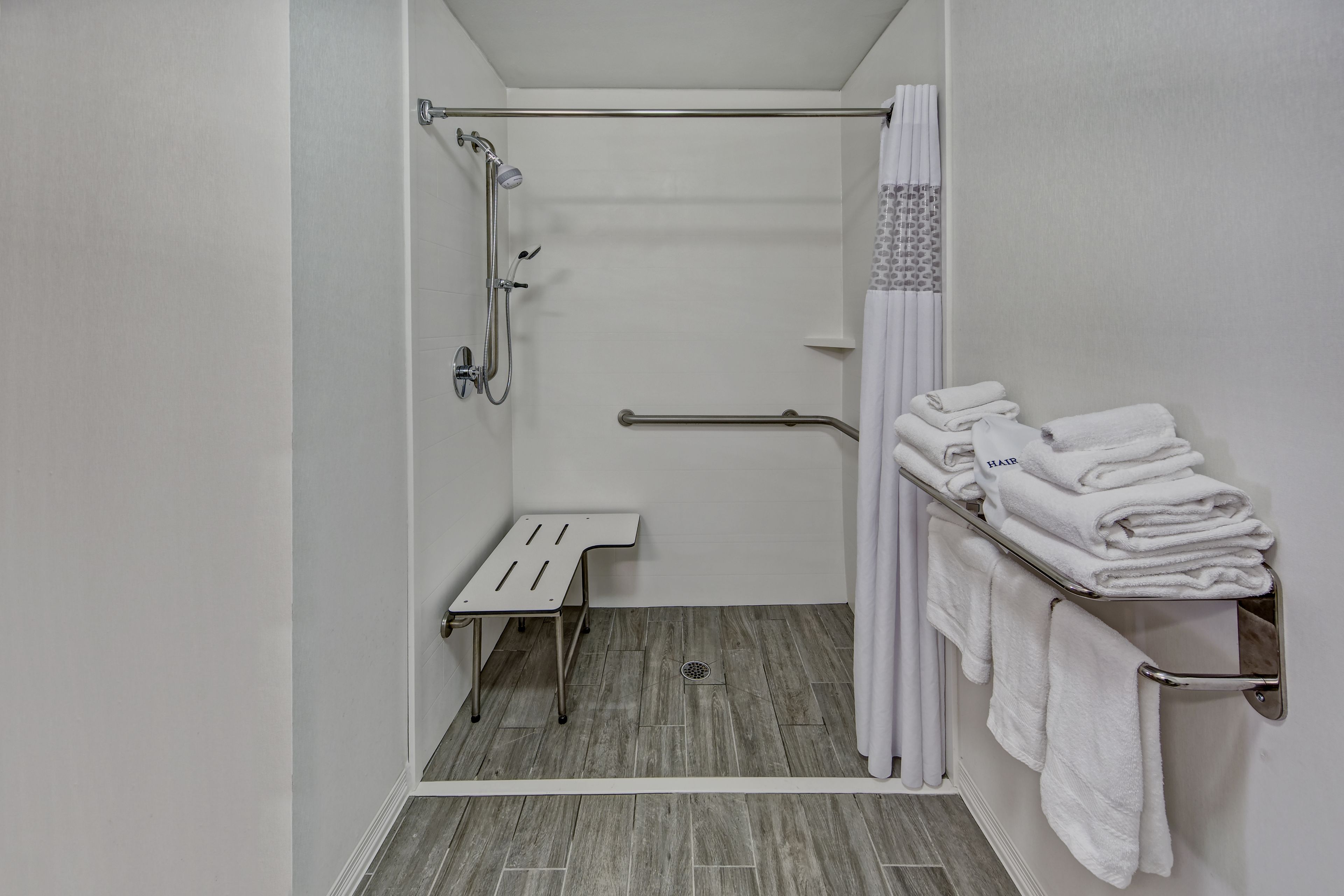 A small, modern bathroom with a shower, grab bar, and a towel rack.