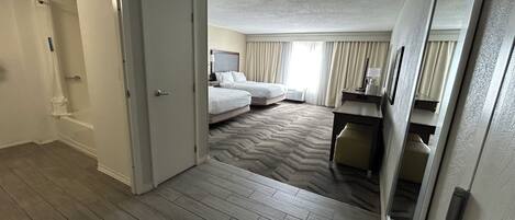 Habitación de hotel con piso de madera, cama, escritorio y baño con ducha e inodoro.