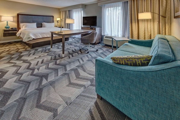 Habitación de hotel con cama, escritorio, silla y sofá color turquesa.
