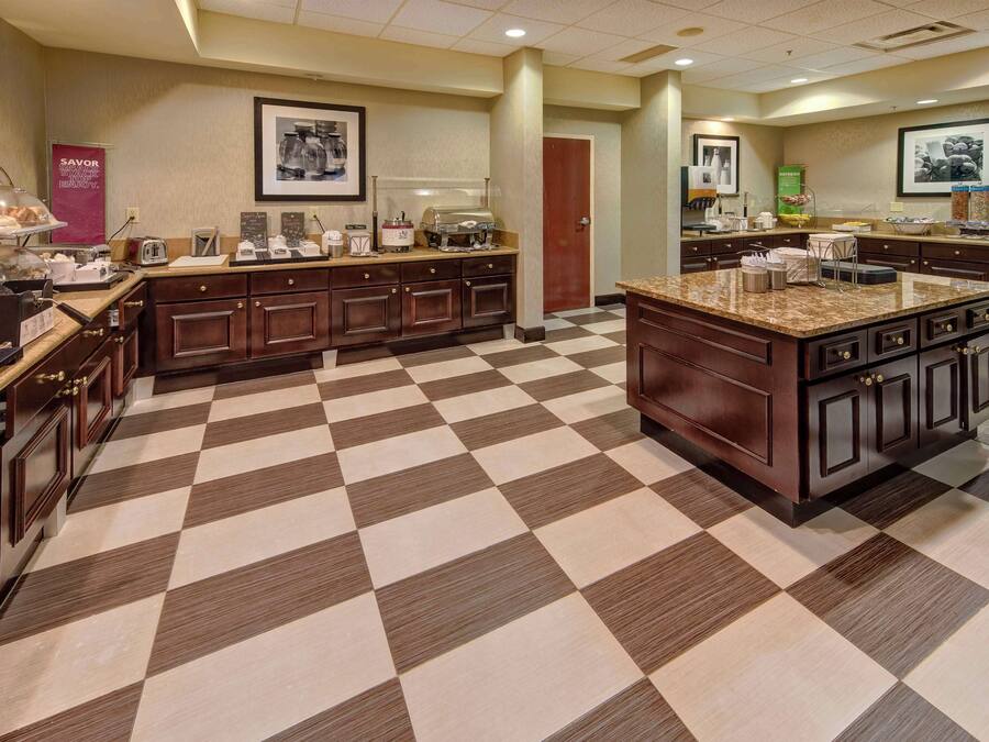 Una cocina de hotel con suelo a cuadros, armarios de madera y diversos electrodomésticos.