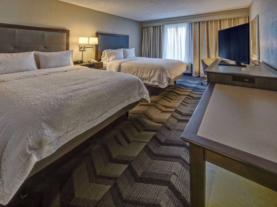 Une chambre d’hôtel avec deux lits, un bureau, un téléviseur à écran plat et une grande fenêtre avec des rideaux.