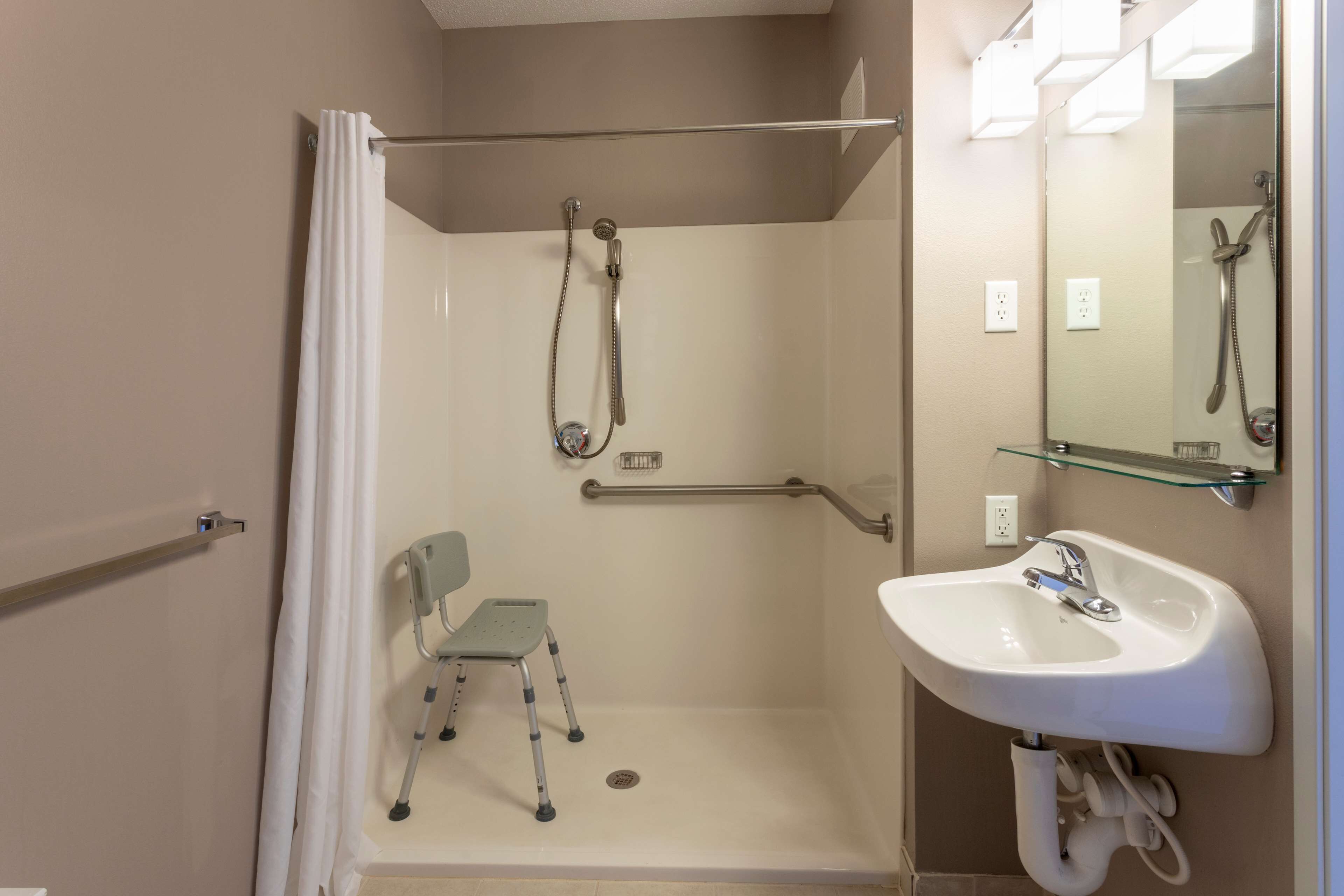 A bathroom with a shower, a wheelchair-accessible chair, and a sink.