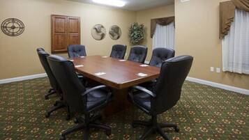 A conference room with a wooden table, six black chairs, a clock, a cabinet, and a plant.