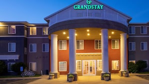 Ein GrandStay Hotel mit zentralem Eingang, Säulen und einem Parkplatz.