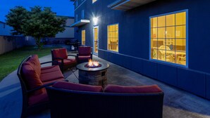 Eine Terrasse im Freien mit Feuerstelle, Korbmöbeln und großen Fenstern.