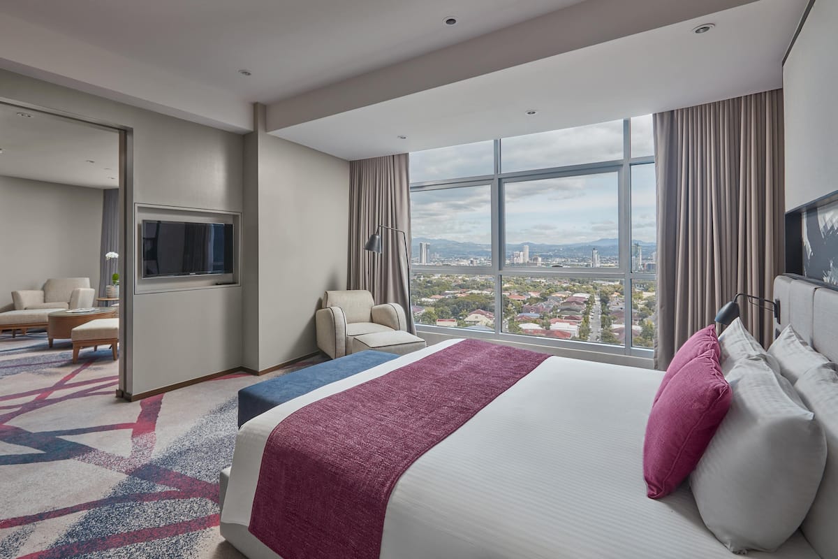 Une chambre d’hôtel avec un grand lit, une télévision, un coin salon et une vue sur la ville.