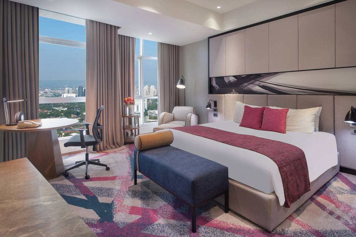 Habitación de hotel moderna con una cama grande, un escritorio y vistas a un paisaje urbano.