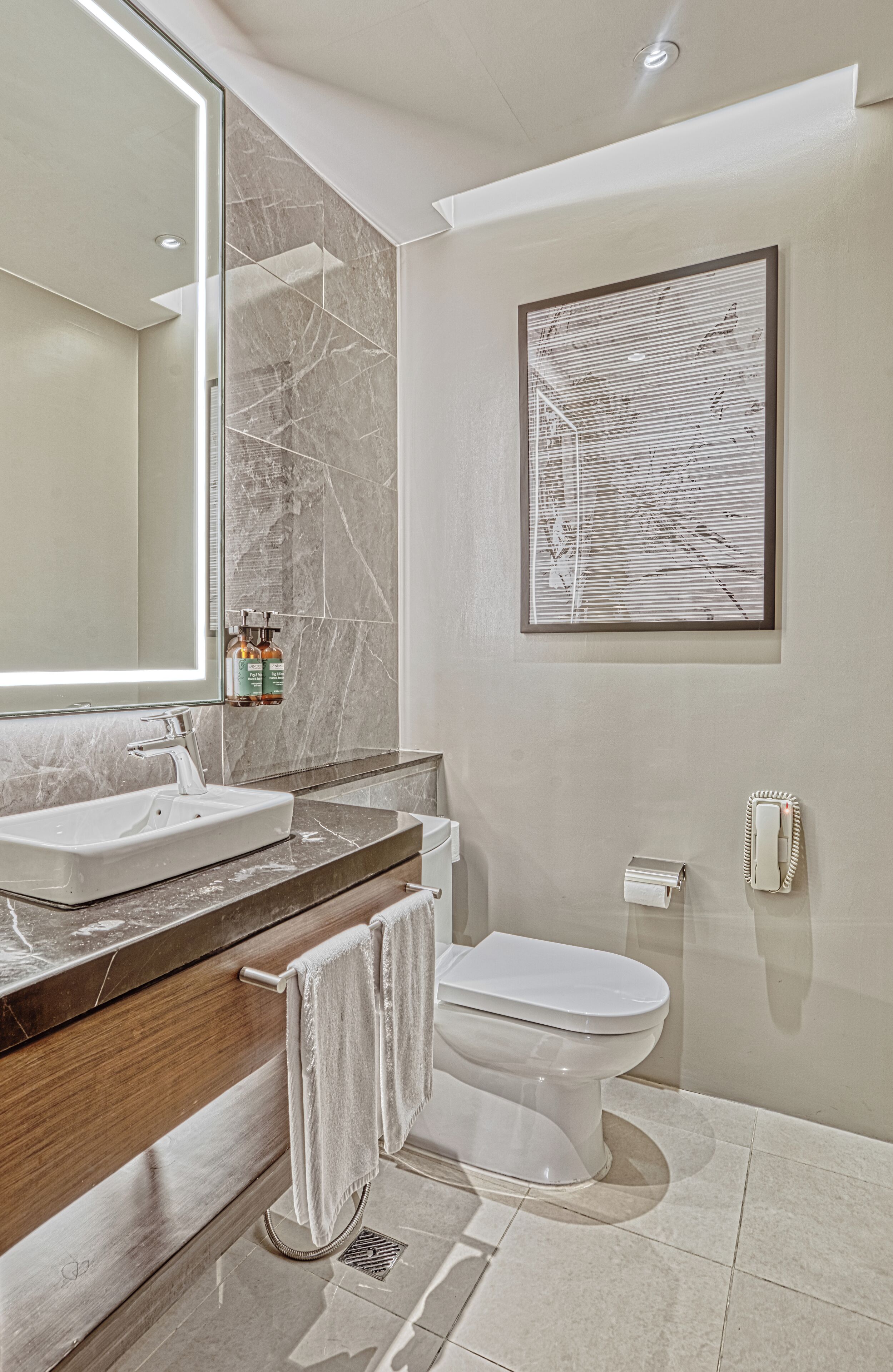 Une salle de bain moderne avec un grand miroir, des carreaux de marbre, un lavabo blanc et des toilettes.