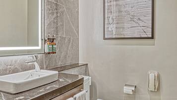 A modern bathroom with a large mirror, marble tiles, a white sink, and a toilet.