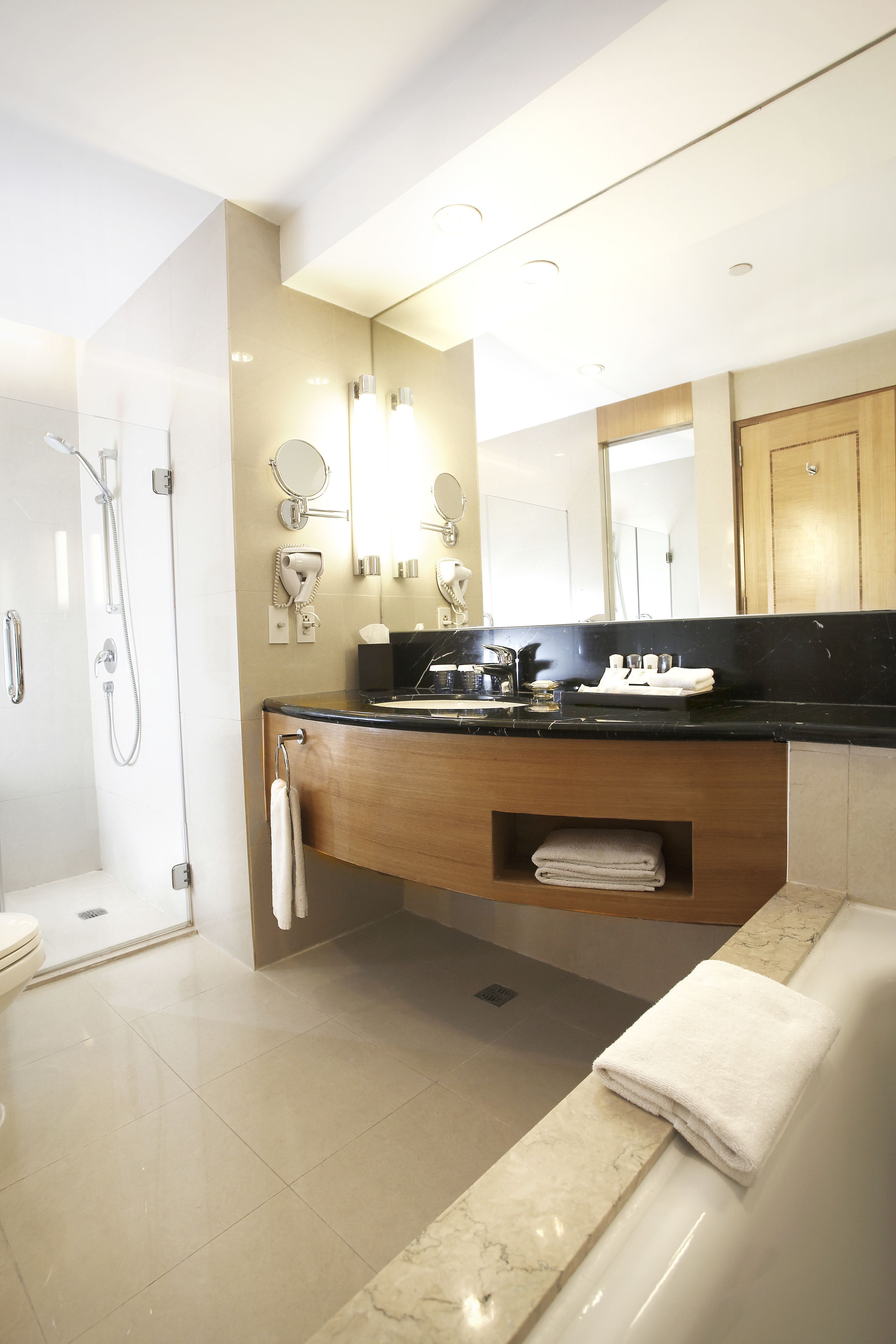 Un bany modern amb dutxa, vàter i banyera. Inclou un lavabo amb mirall, un suport per a tovalloles i una estant amb tovalloles plegades.