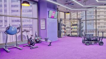 A gym with purple walls, exercise equipment, and a view of buildings through large windows.