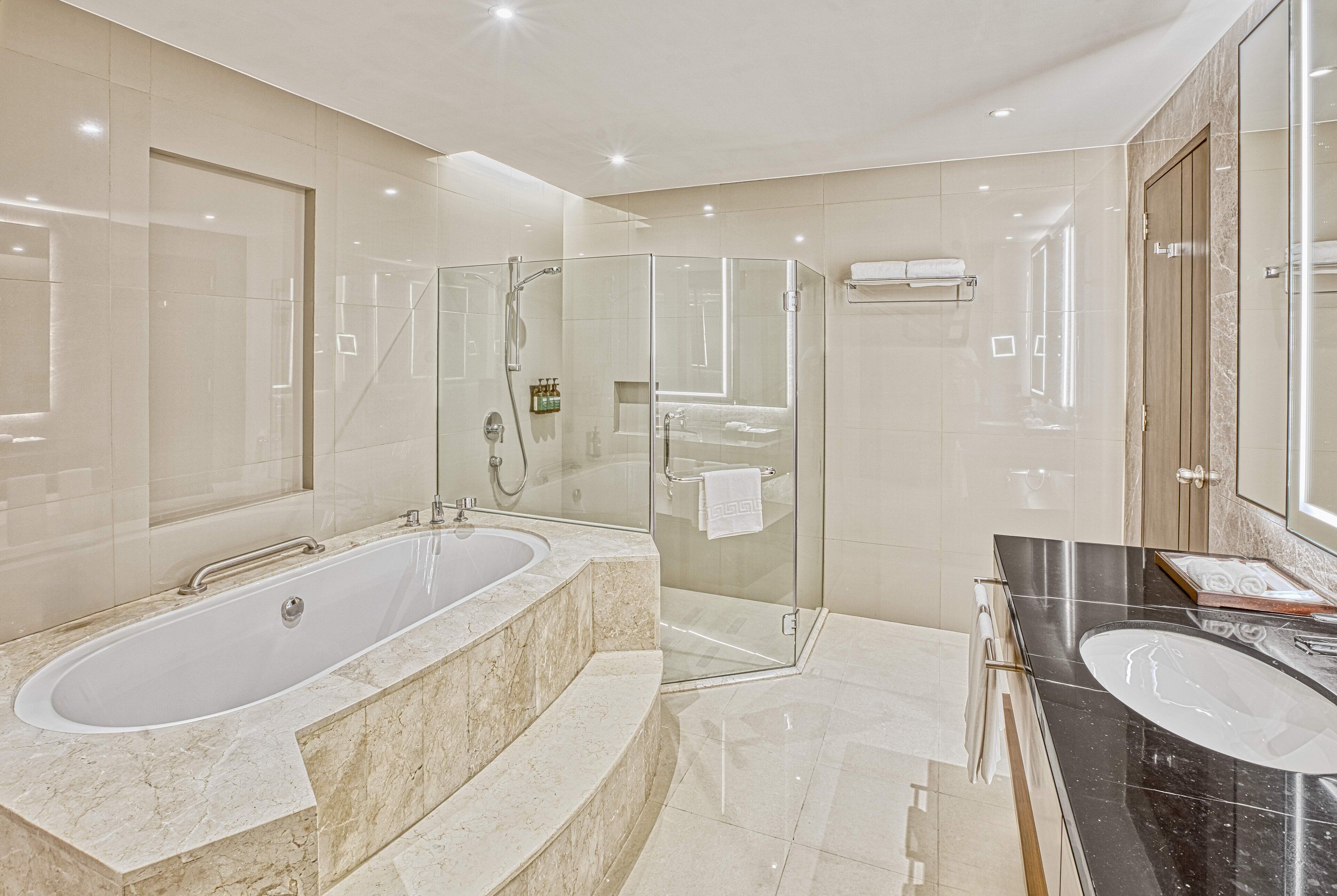 Une salle de bain moderne dotée d’une douche à parois de verre, d’une grande baignoire sur pied et d’un meuble-lavabo séparé avec un plan de travail noir.