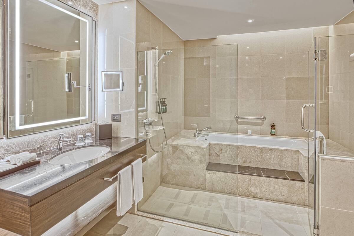 Un baño moderno con un espejo grande, dos lavamanos, una bañera y un box de ducha de vidrio.