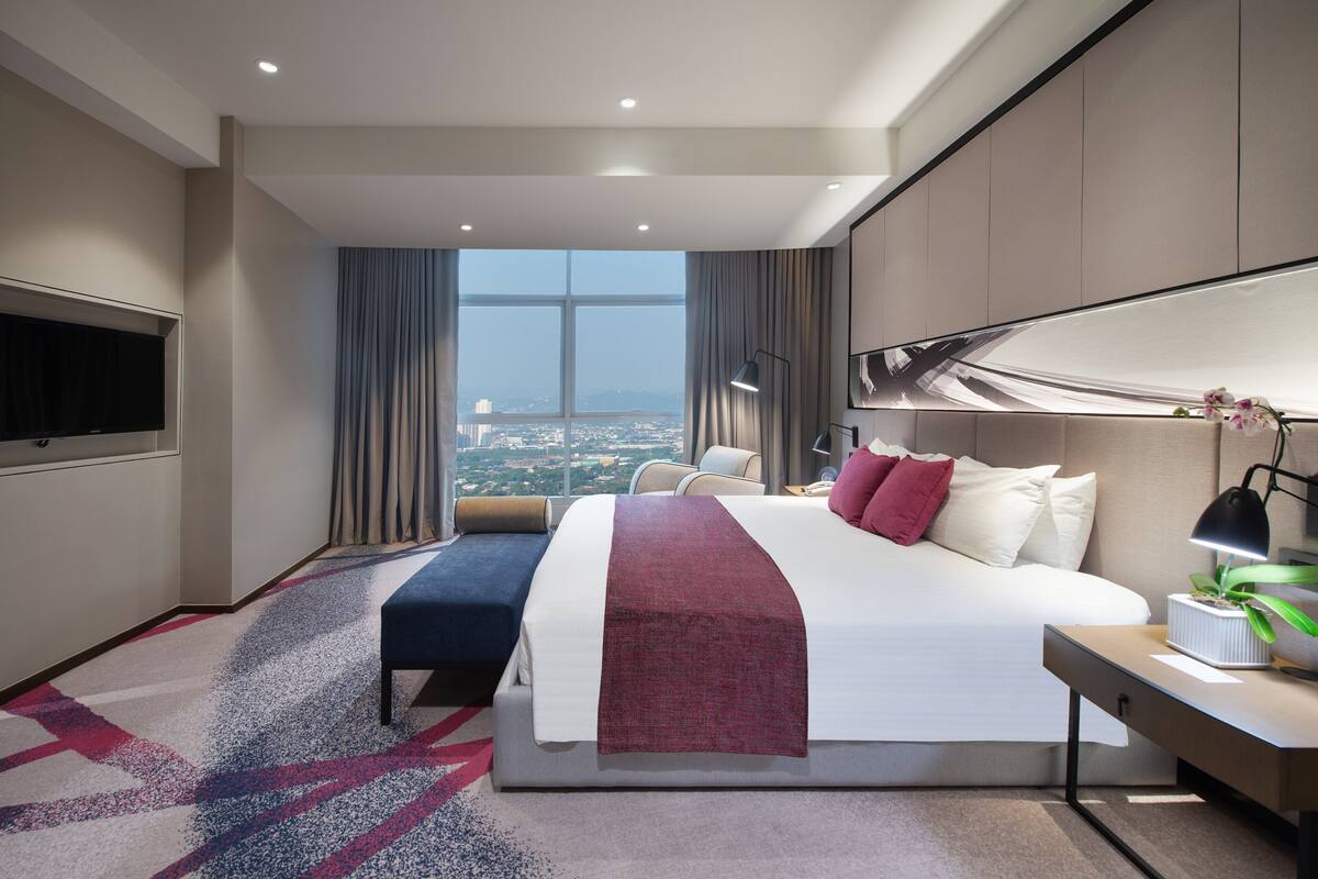 Una habitación de hotel moderna con una cama grande, un escritorio, un televisor de pantalla plana y vistas a la ciudad a través de la ventana.