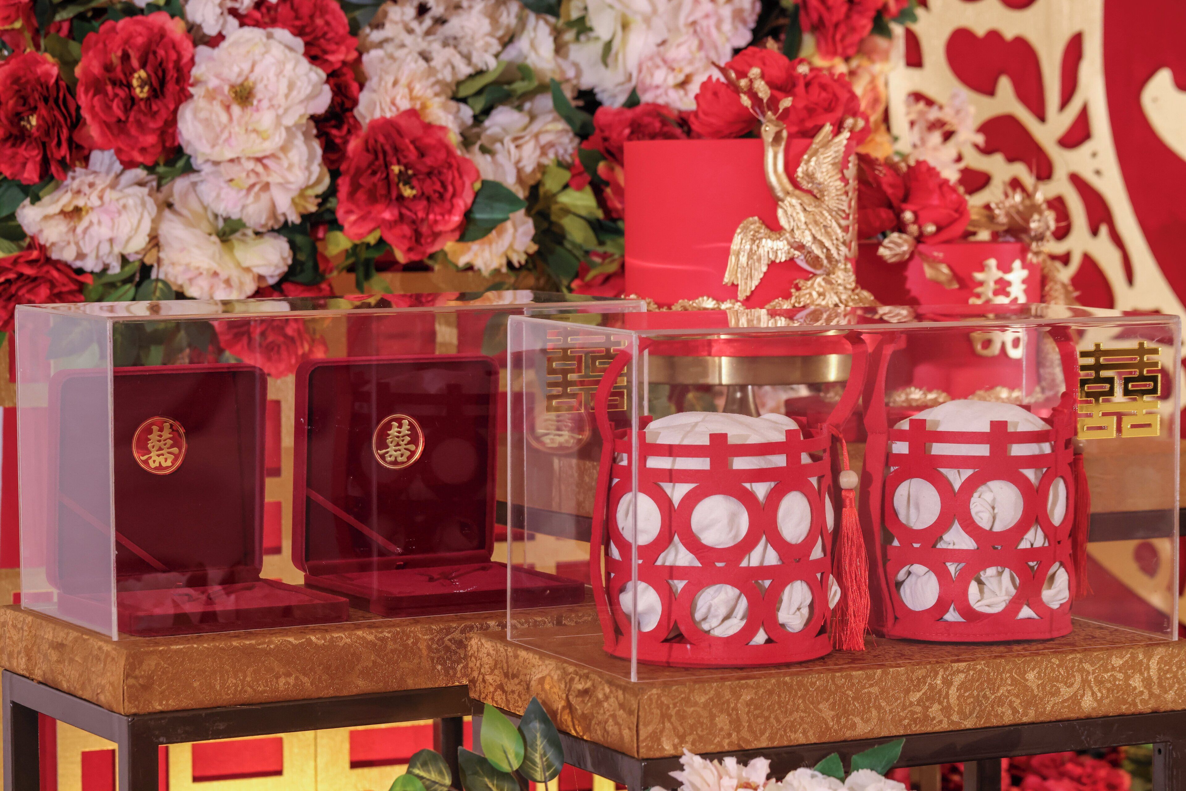 A display of traditional Chinese decorative items, including red and white ceramic containers with intricate designs, set against a backdrop of red and white flowers.
