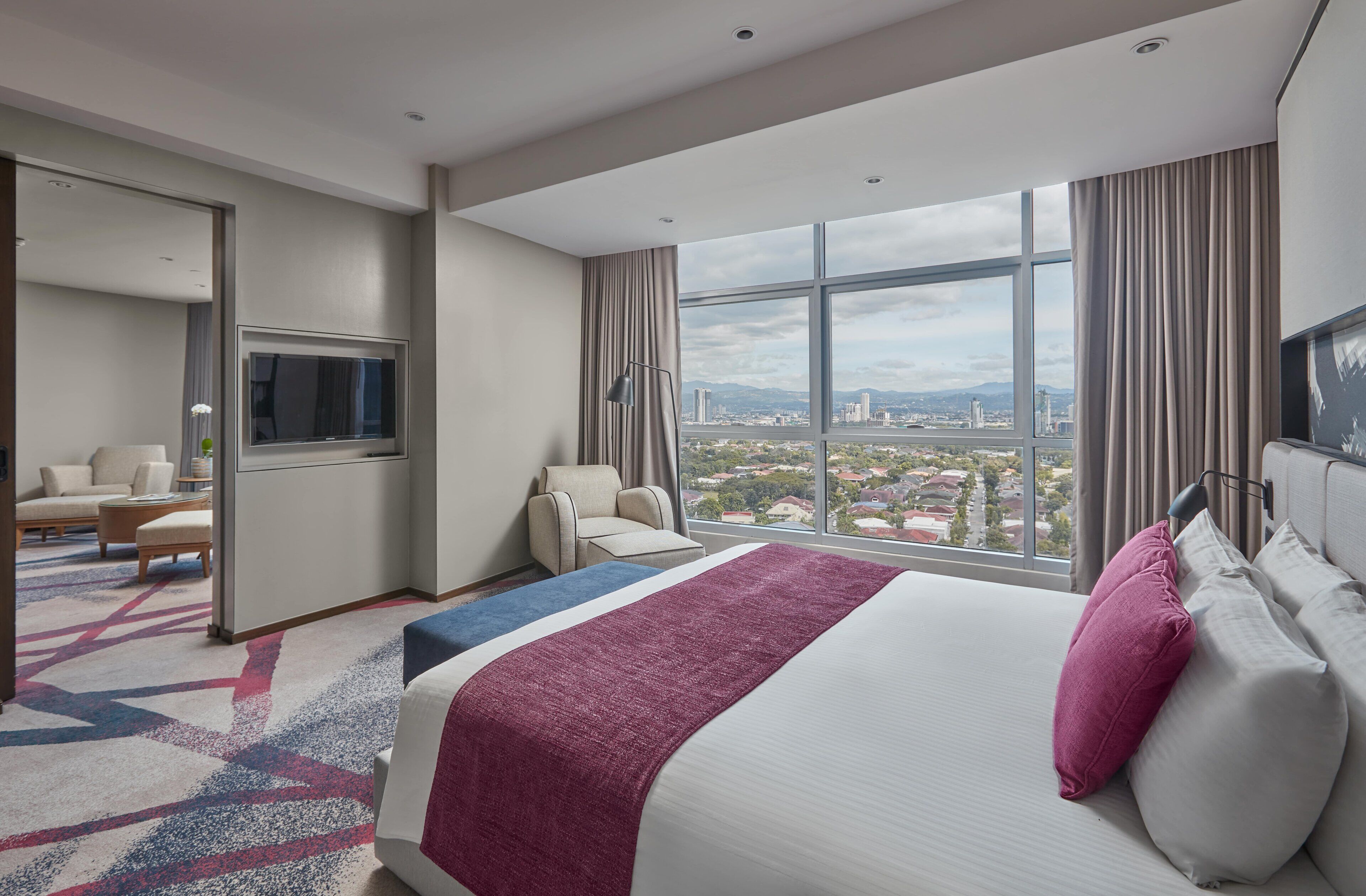 Une chambre d’hôtel avec un grand lit, une télévision, un coin salon et une vue sur le paysage urbain.