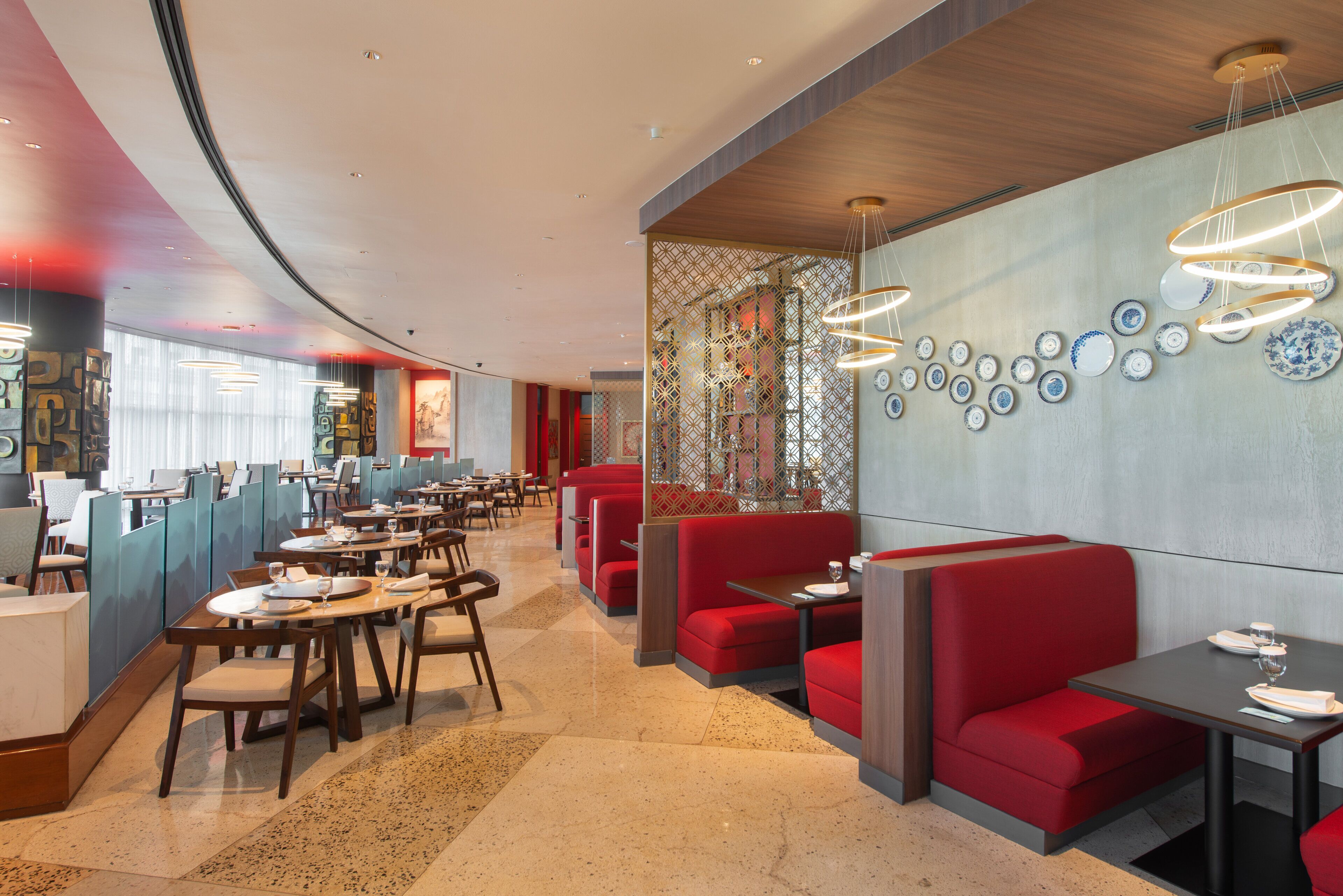 A modern restaurant interior with booths and tables, a patterned wall, and a series of hanging light fixtures.